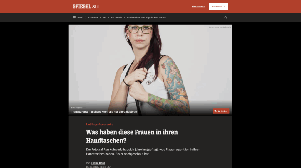 Frau mit grüner Brille und buntem Ganzarm-Tattoo, die eine schwarze Schultertasche vor einem hellen Hintergrund hält.