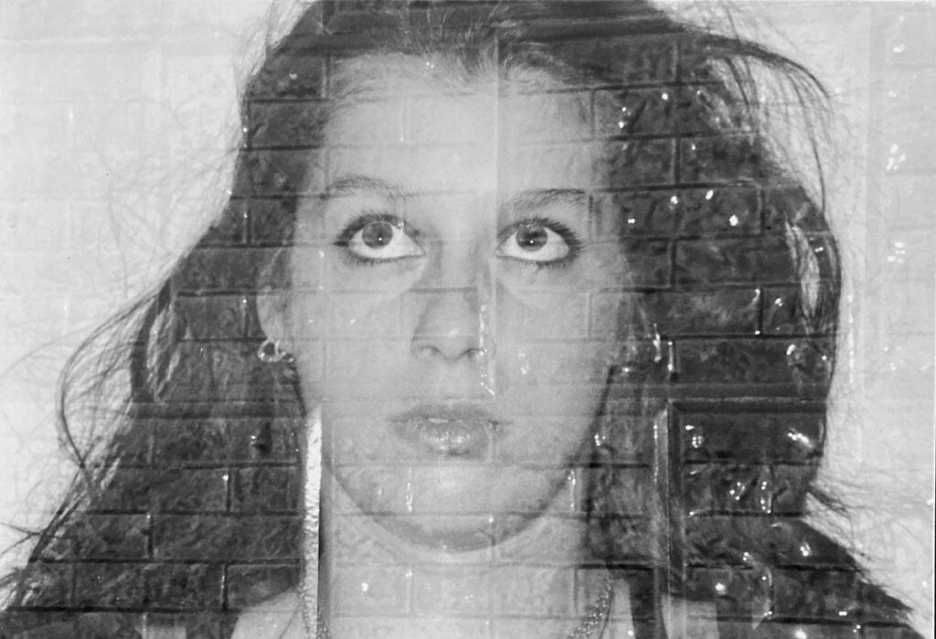 Schwarz-weiß-Doppelbelichtung eines nach oben schauenden Frauenporträts mit langen lockigen Haaren, überlagert von dem Muster einer Backsteinwand